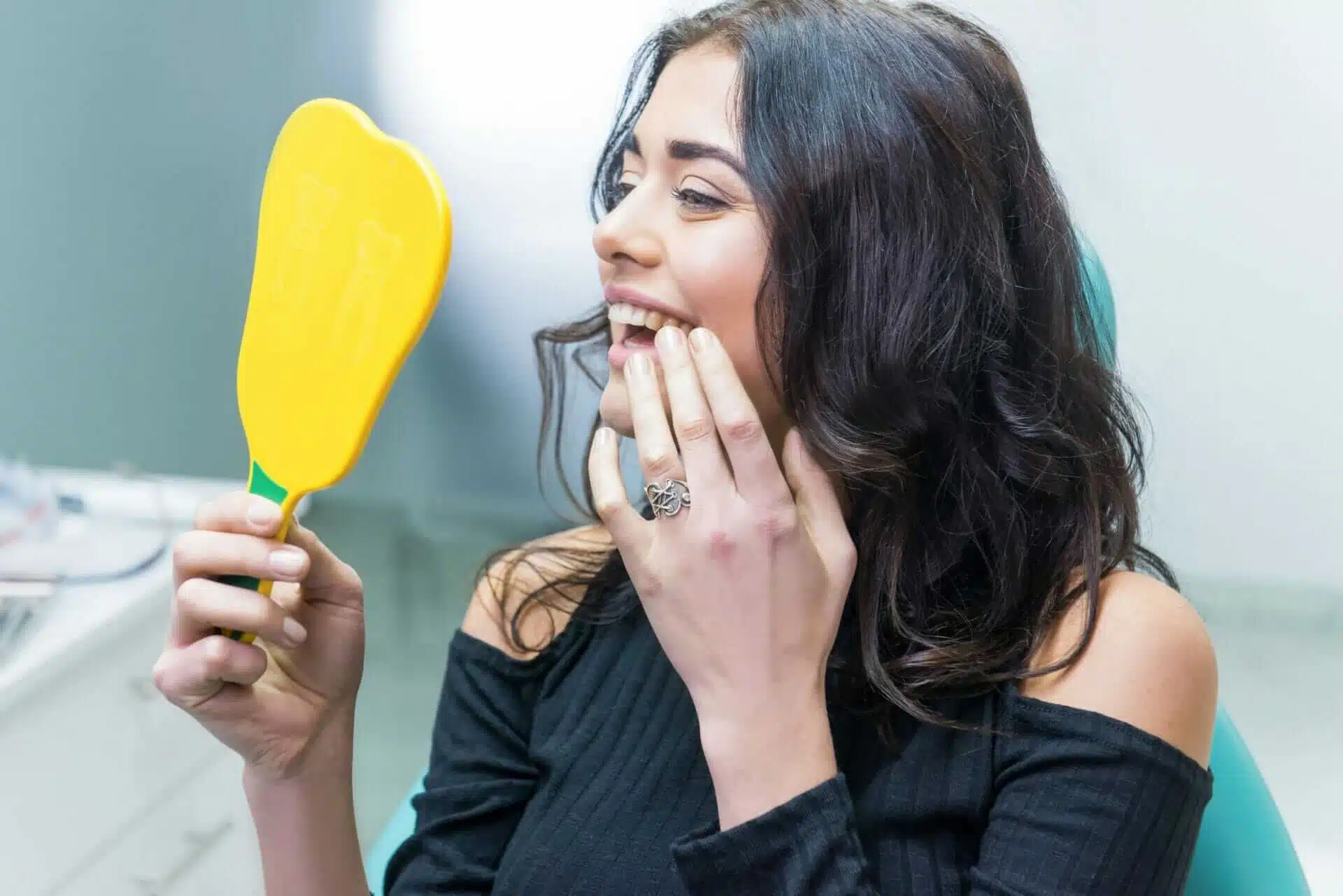 Happy patient admiring her smile in a dental mirror at Southern Style Dental office. Quality dental care for beautiful smiles.