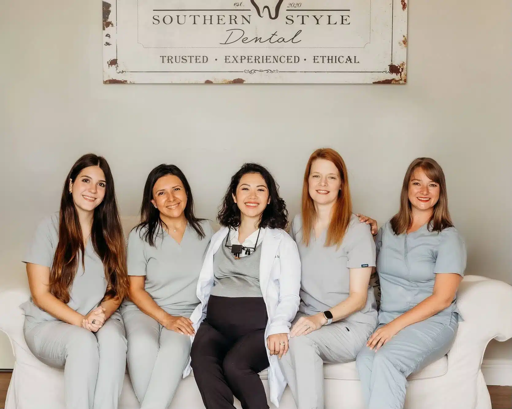 Dental team at Southern Style Dental, trusted experienced ethical care, seated in front of clinic sign.