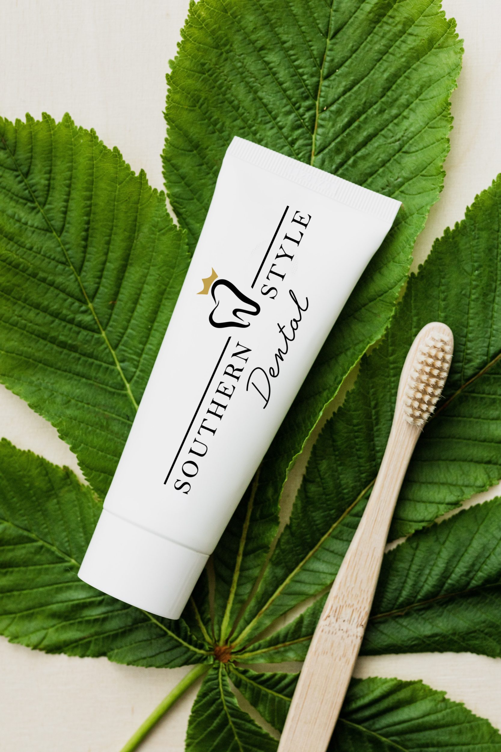 Toothpaste tube and bamboo toothbrush on green leaves